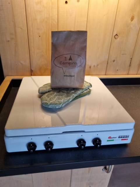 Bolsa de papel y guantes de cocina sobre una estufa en una carpa safari con paredes de madera.