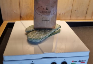 Paper bag and oven mitts on a stove in a wood-paneled safari tent at a campsite in the Netherlands.