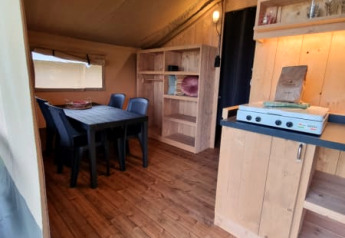 Interieur van een safaritent met houten meubilair en eettafel bij Camping de Tulpenweide in Nederland.