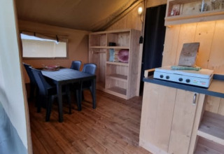 Interior de una tienda safari con muebles de madera y mesa de comedor en Camping de Tulpenweide, Países Bajos.