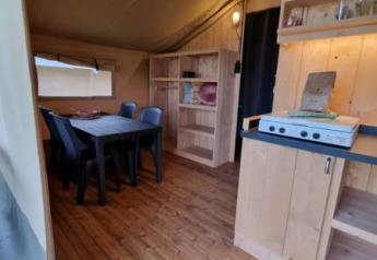 Interno di una tenda safari con mobili in legno e tavolo da pranzo a Camping de Tulpenweide, Paesi Bassi.