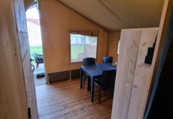 Vista interior de una tienda safari con suelo de madera y mesa en Camping de Tulpenweide, Países Bajos.