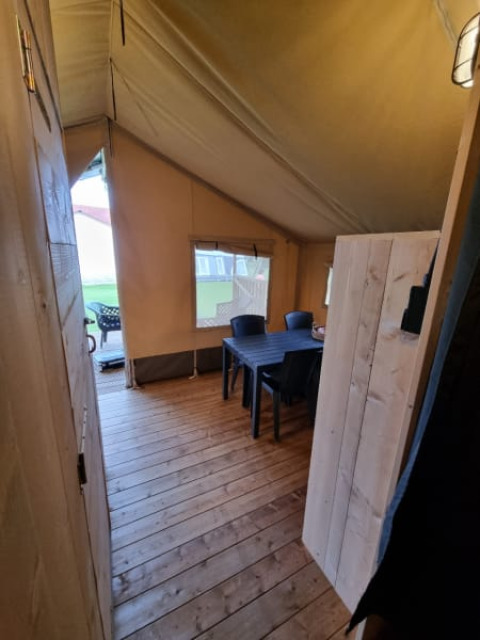 Vista interior de una tienda safari con suelo de madera y mesa en Camping de Tulpenweide, Países Bajos.