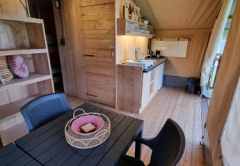Vista interior de una tienda safari con muebles de madera y cocina en Camping de Tulpenweide, Países Bajos.
