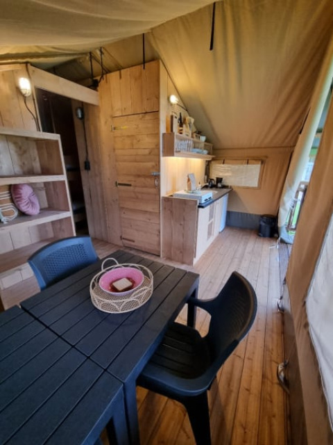 Interieur van een safaritent met houten meubels en kitchenette op Camping de Tulpenweide in Nederland.