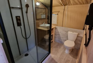 Baño en tienda safari en Camping de Tulpenweide, Países Bajos, con ducha moderna y sanitario visible.