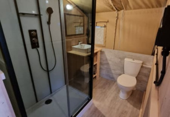 Baño en tienda safari en Camping de Tulpenweide, Países Bajos, con ducha moderna y sanitario visible.