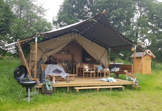 Safari-Zelt mit überdachter Terrasse, Grill und gemütlichen Sitzmöglichkeiten im grünen Naturgebiet.