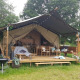 Safari telt med overdækket terrasse, grill og komfortable siddepladser midt i et grønt, skovomgivet område.