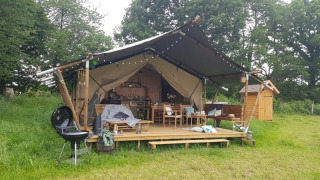 Safari telt med overdækket terrasse, grill og komfortable siddepladser midt i et grønt, skovomgivet område.