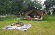 Tente safari à Glamping des 2 Marguerites en France, entourée de verdure avec coin pique-nique à l'avant.