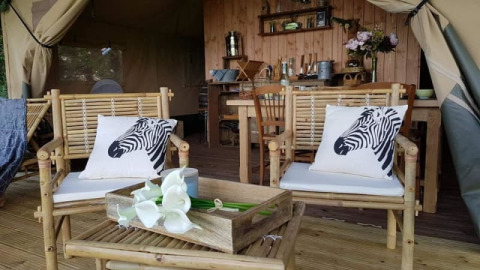 Safari-teltinteriør ved Glamping des 2 Marguerites i Frankrig med bambusmøbler og zebrapuder.