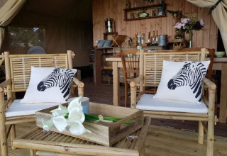 Interior de tienda safari en Glamping des 2 Marguerites, Francia, con sillas de bambú y cojines de cebra.