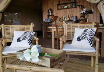 Interno tenda safari al Glamping des 2 Marguerites in Francia, con sedie in bambù e cuscini zebra.