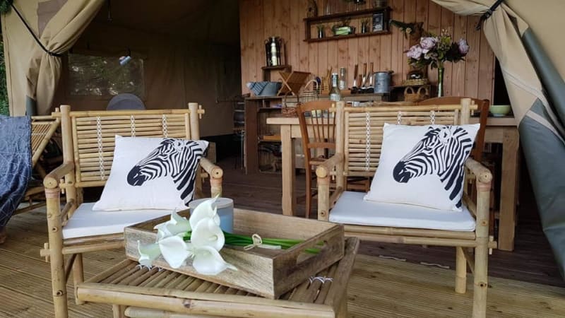 Interior de tienda safari en Glamping des 2 Marguerites, Francia, con sillas de bambú y cojines de cebra.