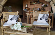 Interno tenda safari al Glamping des 2 Marguerites in Francia, con sedie in bambù e cuscini zebra.