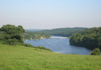 Vista de río tranquilo rodeado de campos verdes y bosque desde la tienda safari en Glamping des 2 Marguerites, Francia.