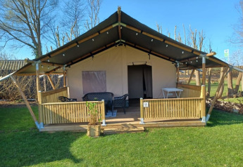 Safari-Zelt mit überdachter Veranda, Sitzmöglichkeiten im Freien und Holzzaun auf einer Wiese.
