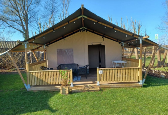 Safari tent with a covered porch, outdoor seating, and wooden fencing set on a grassy field.