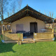 Tienda safari con porche cubierto, asientos exteriores y valla de madera sobre un césped verde.