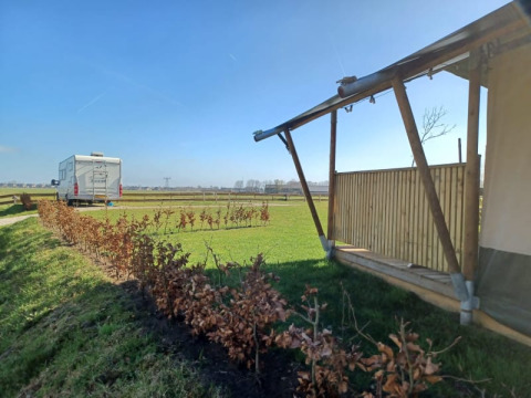 Tienda safari y autocaravana en Camping de Noorde, Países Bajos, con vistas a campos abiertos y cielo azul.