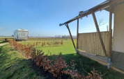 Tienda safari y autocaravana en Camping de Noorde, Países Bajos, con vistas a campos abiertos y cielo azul.