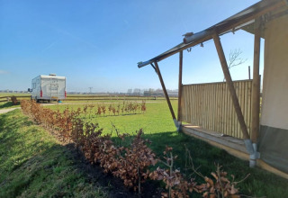 Safaritent en camper op Camping de Noorde in Nederland met zicht op open velden en blauwe lucht.