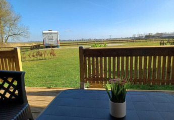 View from a safari tent terrace at Camping de Noorde, Netherlands, overlooking grass lawn and campervan.