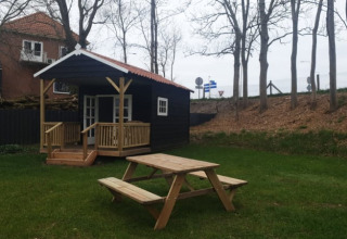Safari-Zelt bei Camping de Noorde in den Niederlanden mit Holzhütte, Picknicktisch und Bäumen im Garten.