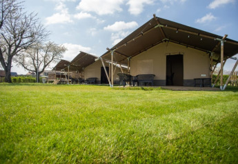 Safari tents positioned on a green lawn under a blue sky with scattered clouds and trees in the background.