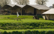 Tienda safari en Camping de Boomgaard, Bélgica, rodeada de césped verde y área de descanso exterior.