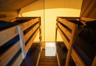 Interno di tenda safari con due letti a castello e luce soffusa al Camping de Boomgaard, Belgio.