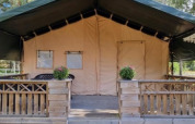Tienda safari con terraza y escalera de madera, situada entre árboles, ideal para glamping en la naturaleza.