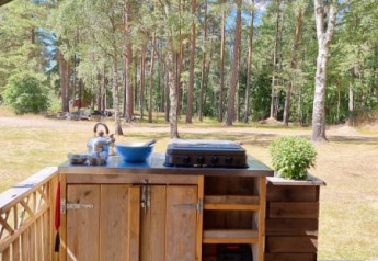 Cocina exterior en una tienda safari con instalaciones sanitarias, rodeada de árboles en un bosque soleado.