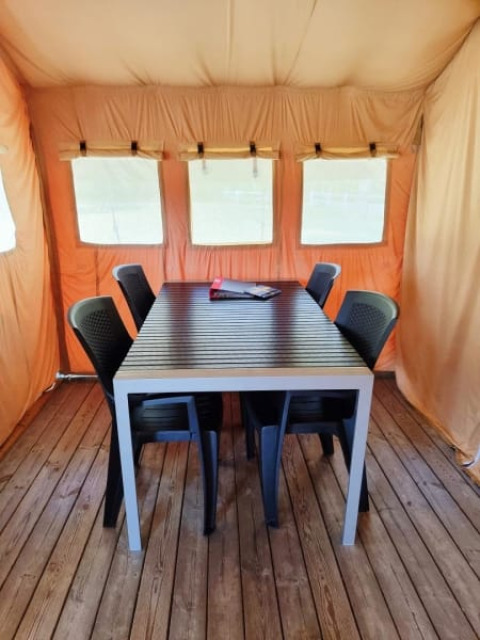 Binnenzicht van Safari tent + sanitair met houten vloer, tafel, zes zwarte stoelen en oranje tentdoek.