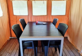 Binnenzicht van Safari tent + sanitair met houten vloer, tafel, zes zwarte stoelen en oranje tentdoek.