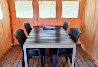 Interior de la tienda Safari + sanitario con suelo de madera, mesa, seis sillas negras y paredes naranjas.
