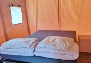 Vista interior de una tienda safari mostrando una cama con sábanas y almohadas blancas sobre suelo de madera.