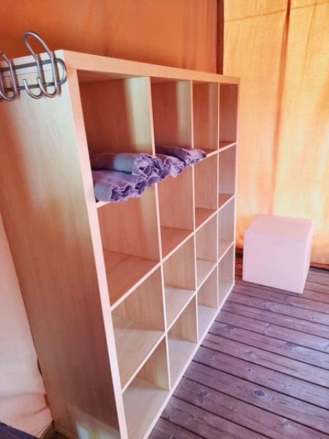 Opbergvak met handdoeken in een safaritent op houten planken en veel natuurlijk licht.