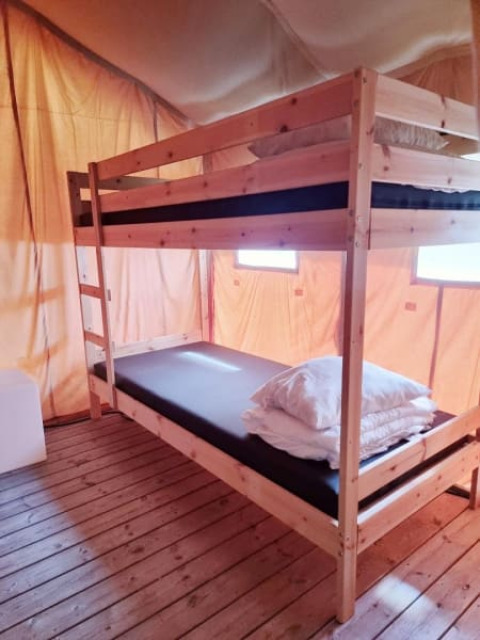 Binnenkant van een safaritent met houten stapelbed, matrassen en kussens op houten vloer.