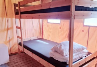 Interior de una tienda safari con literas de madera, colchones y almohadas sobre suelo de madera.