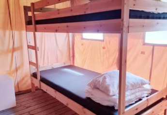Interior de una tienda safari con literas de madera, colchones y almohadas sobre suelo de madera.
