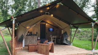 Safari tent with sanitary facilities, wooden deck and furniture set in a lush green forested area.