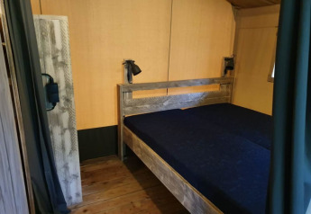 Bedroom with wooden floor and double bed in a safari tent with private sanitary at a Dutch campsite.