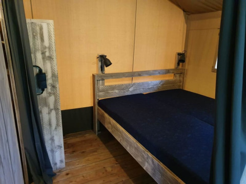 Bedroom with wooden floor and double bed in a safari tent with private sanitary at a Dutch campsite.