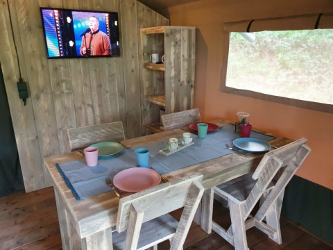 Eethoek in safaritent met houten tafel, gekleurd servies, tv en raam bij Camping het Horstmannsbos, Nederland.
