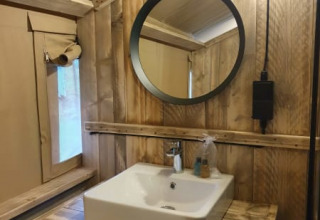 Baño con paredes de madera rústica y lavabo cuadrado en una tienda safari en Camping het Horstmannsbos.