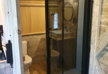 Bathroom inside a safari tent featuring a glass shower, toilet, and sink at Camping het Horstmannsbos, Netherlands.