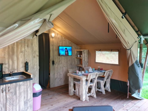 Interior of a luxury safari tent with wooden furniture, kitchen, and TV at Camping het Horstmannsbos in the Netherlands.