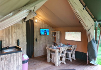 Interno di una tenda safari di lusso con mobili in legno, cucina e TV al Camping het Horstmannsbos nei Paesi Bassi.